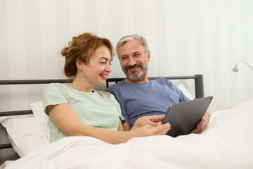 Smiling mature couple using digital tablet at home in bed