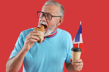 Senior man with flag of France and coffee cup eating croissant on red background