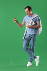 Young man with tape measure on green background