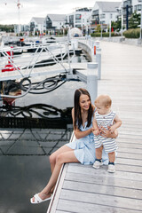 Happy young mother and her little son spend time outdoors. A young mother smiles and holds her son. Mother and child are dressed in summer clothes. Happy motherhood and childhood