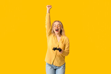Cheerful young woman with game pad celebrating success on yellow background