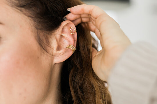 Cropped close-up shot of a young woman with two asymmetrical golden ear cuffs. Female with golden ear cuffs, side view.