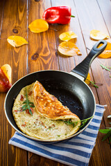 Fried omelets with various autumn vegetables in a frying pan on a wooden table.