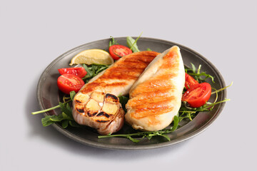 Plate of tasty grilled chicken breast with arugula, tomatoes and garlic on white background