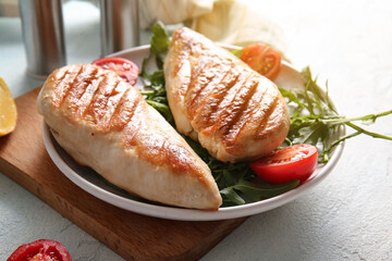 Plate of tasty grilled chicken breast with arugula and tomatoes on light blue background