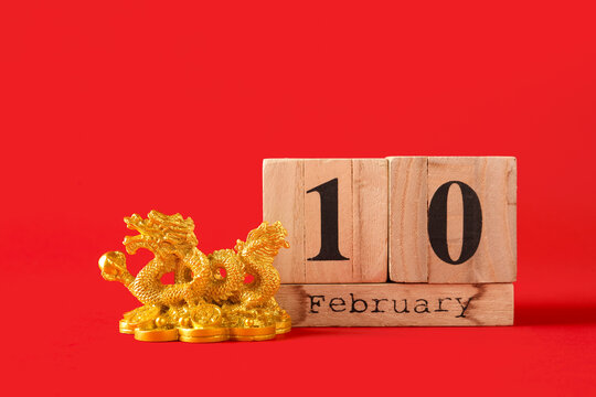 Golden dragon figurine and cube calendar with date 10 FEBRUARY on red background, closeup. Chinese New Year celebration