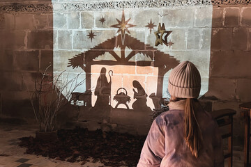 A child looks at christmas creche with Joseph Mary and small Jesus in a crib