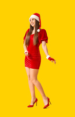 Young woman in Santa hat on yellow background