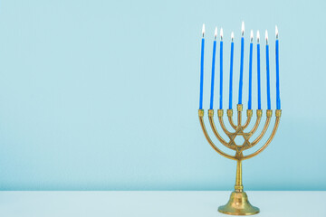 Menorah with burning candles on white table near blue wall, closeup. Hanukkah celebration