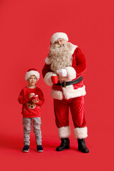 Santa Claus and cute little boy with cups of hot chocolate on red background
