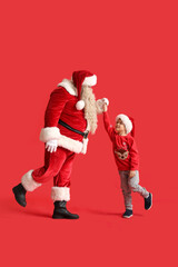 Santa Claus and cute little boy dancing on red background