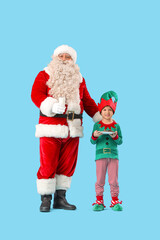 Santa Claus and cute little elf with milk and cookies on blue background