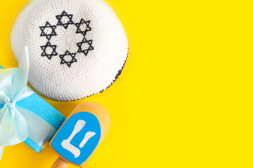 Dreidel, kippah and gift box for Hanukkah celebration on yellow background