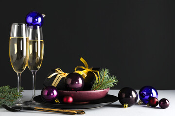 Beautiful table setting with glasses of champagne, Christmas gifts and decorations on light table against dark background