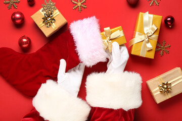 Obraz na płótnie Canvas Santa Claus putting gifts into Christmas sock on red background, closeup