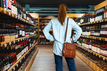 Rear view of woman consumer standing in the liquor store and chooses wine.