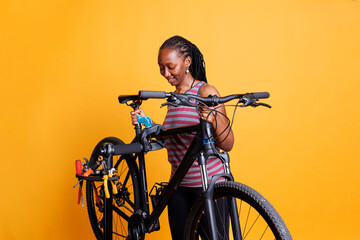 Healthy active african american female does annual bicycle repairs using specialized work tools. Youthful black woman grasping a broken bike to be examined and adjusted on a repair stand.