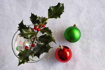 Top down view of one red and one green Christmas bulb ornament with holly branch and red berries...