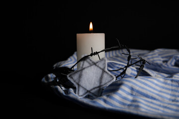 Burning candle with barbed wire, Jewish badge and prisoner uniform on dark background....