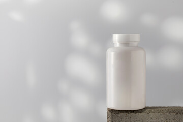  Mockup is a white jar with pills or vitamins on a podium. Medical preparations. Copy space