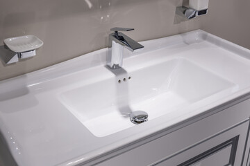 White ceramic sink with chrome faucet in the bathroom. White soap holder and liquid soap dispenser on the wall. Objects have clean lines and modern design