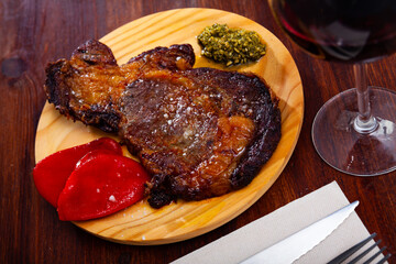 Spicy veal entrecote served with red bell pepper and salsa verde sauce on wooden board