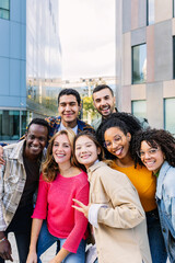Vertical portrait of young group of diverse people smiling at camera outdoors. Happy millennial college students enjoying time together, social gathering and hanging out at city street.