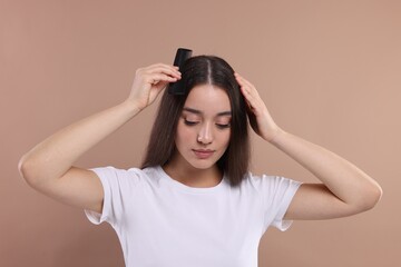 Fototapeta premium Woman with comb examining her hair and scalp on beige background. Dandruff problem