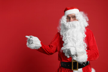 Fototapeta na wymiar Merry Christmas. Santa Claus pointing at something on red background, space for text