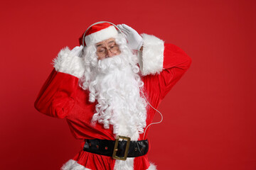 Merry Christmas. Santa Claus in headphones listening to music on red background, space for text