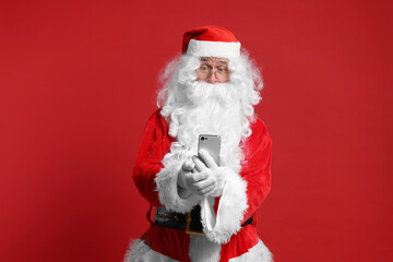 Merry Christmas. Santa Claus using smartphone on red background
