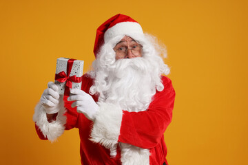 Santa Claus holding Christmas gift on orange background