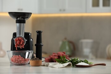 Electric meat grinder with beef mince, parsley, salt and peppercorns on white table in kitchen