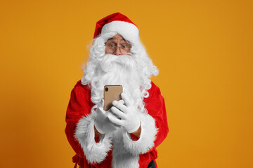 Fototapeta na wymiar Merry Christmas. Santa Claus using smartphone on orange background