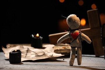 Voodoo doll pierced with pins and ceremonial items on wooden table against blurred background - obrazy, fototapety, plakaty