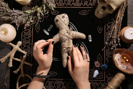 Woman stabbing voodoo doll with needle at table, closeup. Curse ceremony