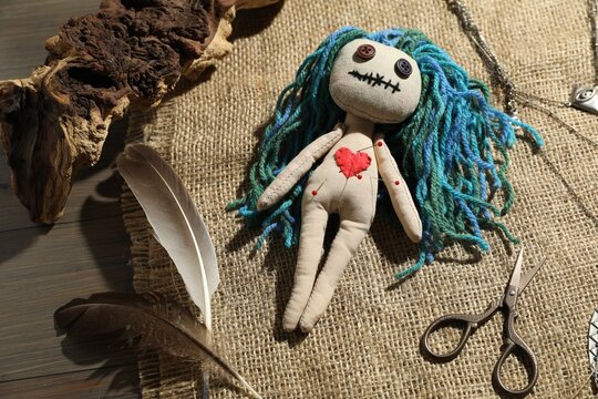 Voodoo doll with pins surrounded by ceremonial items on wooden table