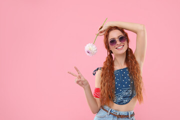 Stylish young hippie woman with dahlia flower showing V-sign on pink background, space for text