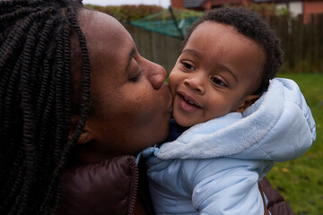 Fototapeta premium Loving mother kisses her son whilst they play outdoors