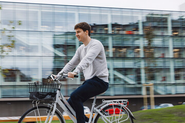 Bike Commuter Young student In City Setting. Green transport, riding bike transport concept. Bike rental system. Modern glass building in background.