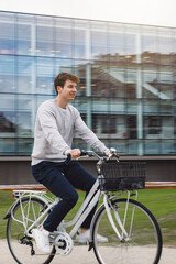 Fototapeta na wymiar Bike Commuter Young student In City Setting. Green transport, riding bike transport concept. Bike rental system. Modern glass building in background.