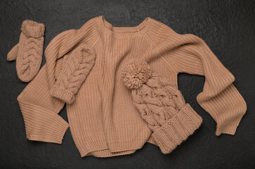 Sweater and winter hat with mittens on concrete background, top view.
