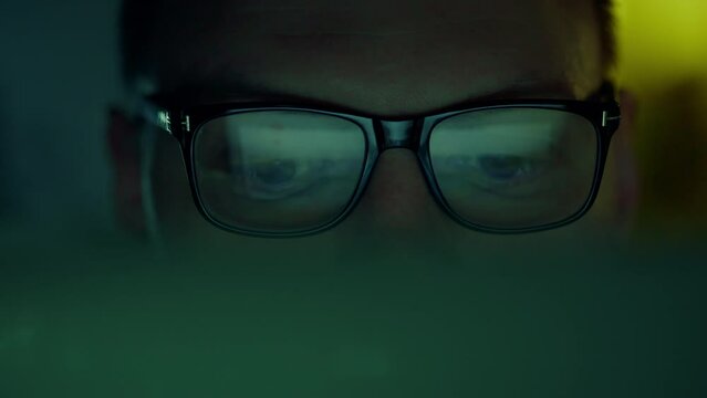 Close-up of a man's eyes, an IT programmer, a man with glasses, peers at the screen with a serious expression on his face. Absorbed in studying and analyzing the information reflected in his glasses