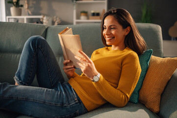 A happy woman is reading a book at cozy home.