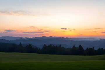 “朝焼けの山並み：オレンジ、ピンク、青のグラデーションが広がる空と、その下に広がる暗青色の山々のシルエット、そして前景には緑の野原が広がる、日の出または日没の風景