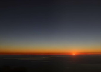 夜明けの地平線に昇るオレンジ色の太陽と青い空のグラデーション