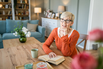 Senior woman mature caucasian female read book at home wear eyeglasses - obrazy, fototapety, plakaty