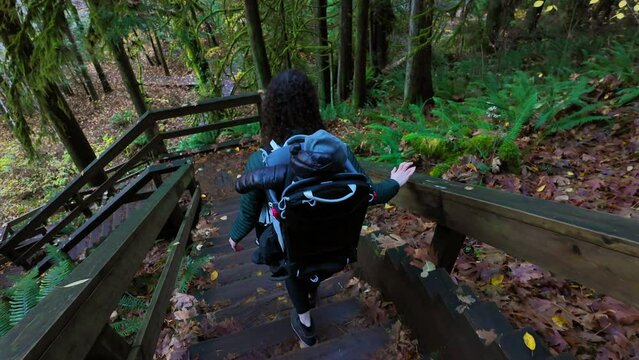 Mother Hiking Down Stairs with Baby in Backpack Carrier in Canadian Nature. Sunny Fall Day, Forest. Lynn Valley, North Vancouver, BC Canada. High quality 4k footage