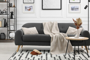 Stylish living room interior with comfortable sofa, blanket, slippers and side table
