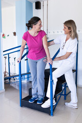 Vertical photo of a physiotherapist stands in the hospital next to her patient as they look at each other and laugh together.